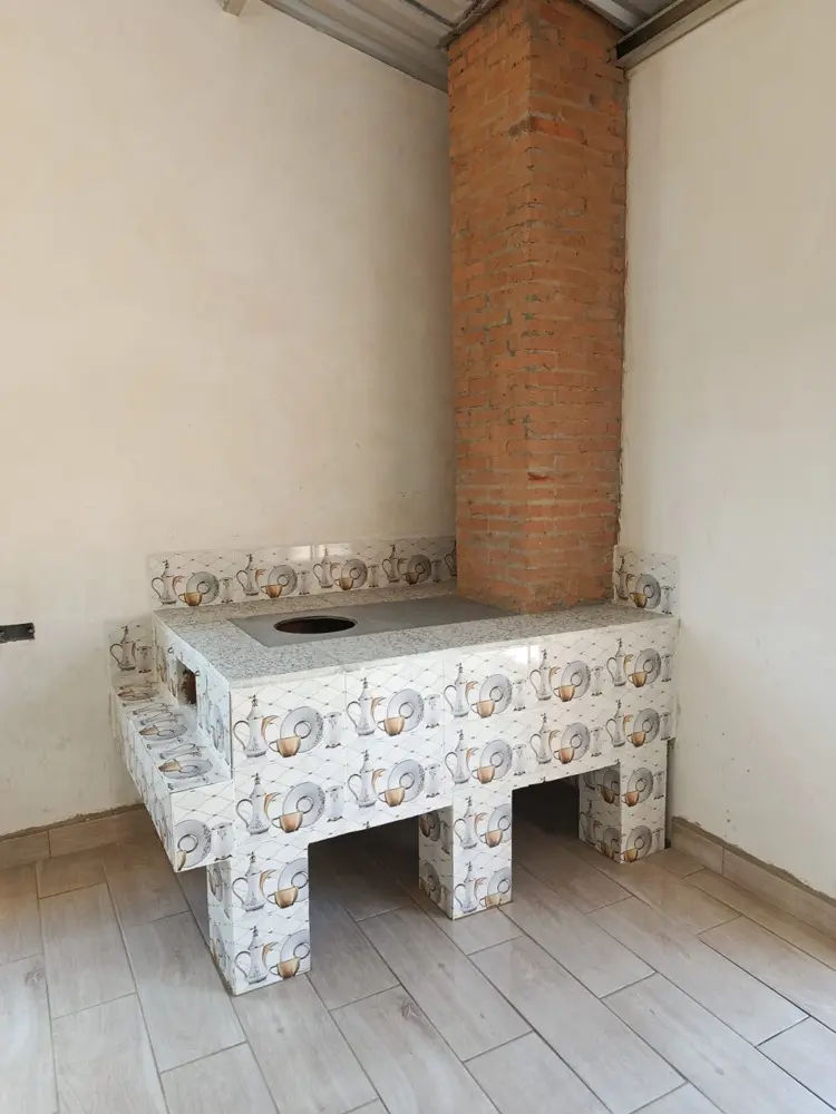 Estufa de le&ntilde;a revestida en azulejo decorado con encimera de granito y chimenea de ladrillo