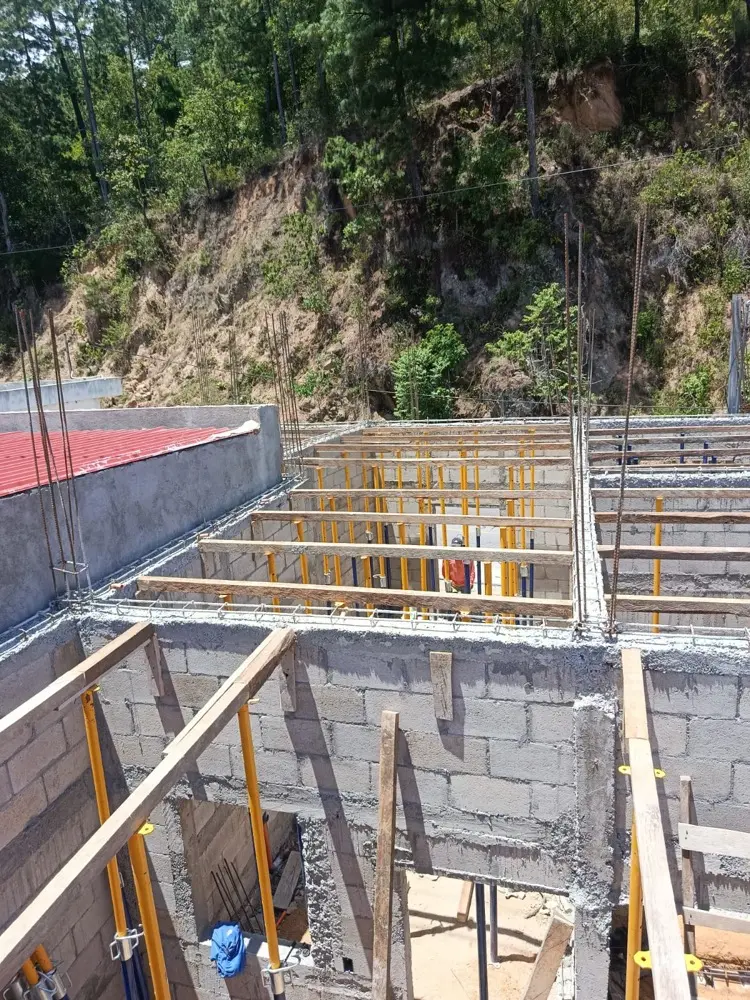 Muros de block con soleras fundidas sobre terreno inclinado, rodeados de pinos